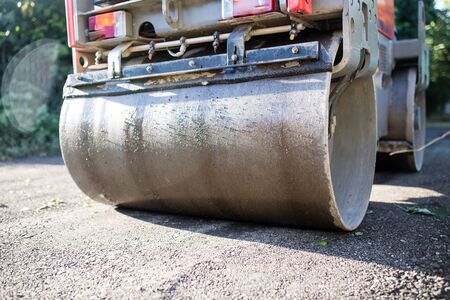 heavy machine rolls a new asphalt road .
