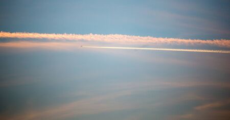 trail from the plane in the sky at sunset .