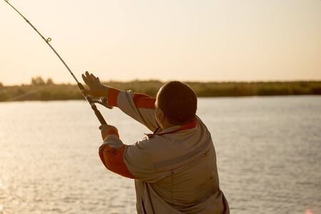 Silhouette of a man with a fishing rod at sunset .
