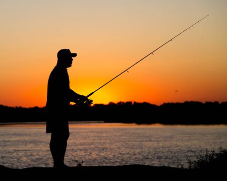 Silhouette of a man with a fishing rod at sunset .の写真素材