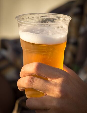 Fresh beer in a plastic cup in the handの写真素材