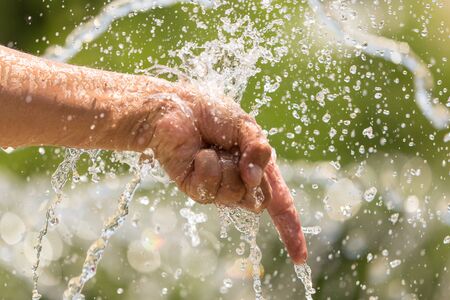 Hand of a man in a spray of water from a fountain .の写真素材