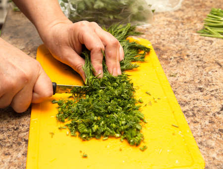 Dill cutting with a knife on the board .の写真素材