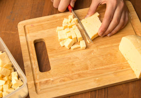 Slicing cheese with a knife on the board .の写真素材