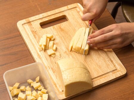 Slicing cheese with a knife on the boardの写真素材