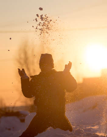 A boy throws snow into the sky at sunsetの写真素材