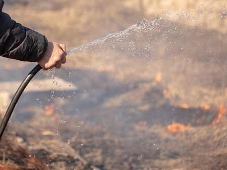 A man extinguishes the burning grass with water .