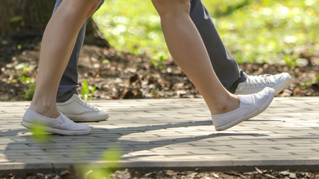 The legs of a girl and a guy are walking along the road in the park