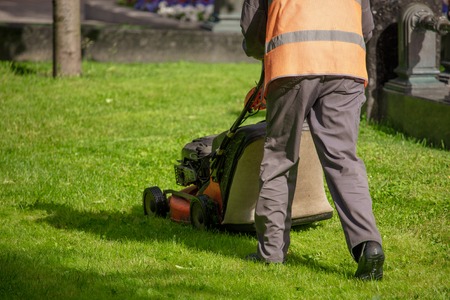 A worker shearing a lawn with a lawn mower in the park