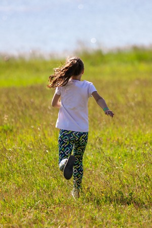 The girl runs along the grass to the meadow .の写真素材