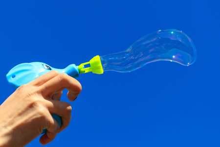 Hand with soap bubbles against the blue sky .