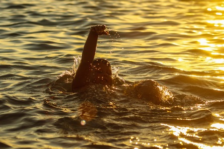 A boy is floating in the sea at sunset .の写真素材