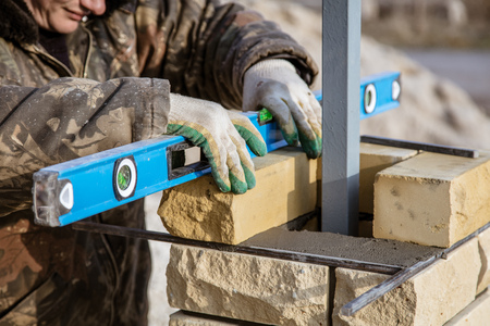 The worker is laying bricks on the fence .