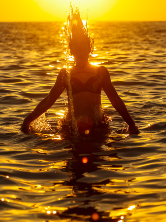 Girl jumps out of the water with splashes at sunset .の写真素材