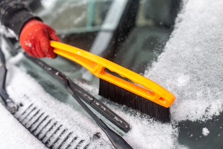 The boy clears snow from a car in the winter .