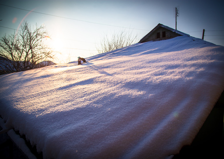 Snow on the roof of the house at sunrise .の写真素材