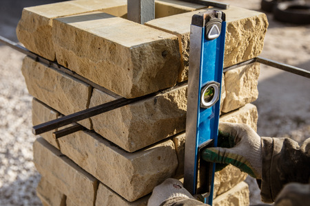 The worker is laying bricks on the fence .