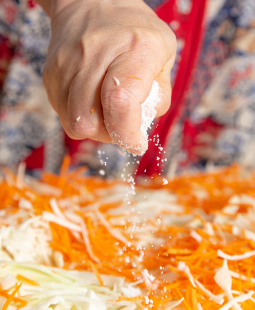 Woman salting cabbage with carrots in the kitchen .の写真素材