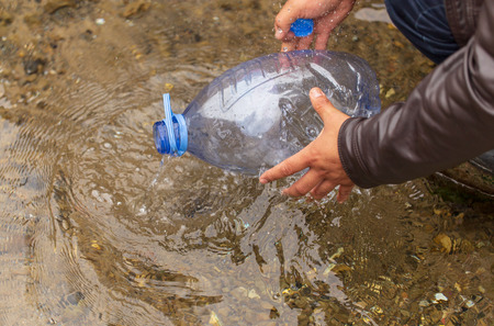 A man collects water in a bottle from a river .