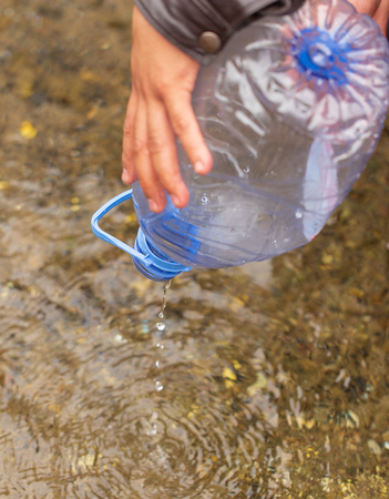 A man collects water in a bottle from a river .の写真素材
