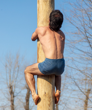 A man climbs a wooden pole against the blue sky.の写真素材