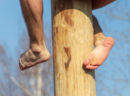 Man's legs on a wooden pole against the blue sky.の写真素材