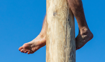Man's legs on a wooden pole against the blue sky.の写真素材