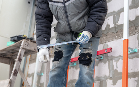 A worker installs a metal profile on the walls of a siding house.
