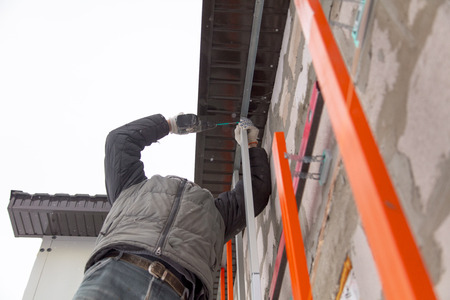 A worker installs a metal profile on the walls of a siding house.