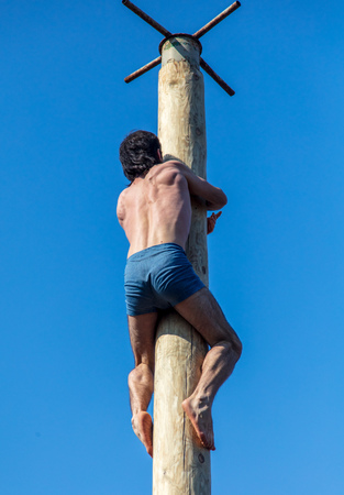 A man climbs a wooden pole against the blue sky.の写真素材