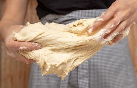 Mistress kneads the dough in the kitchen .