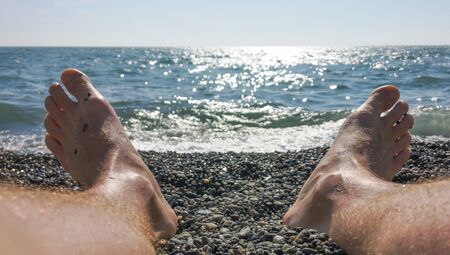 Men's feet on a pebble beach by the sea .の写真素材