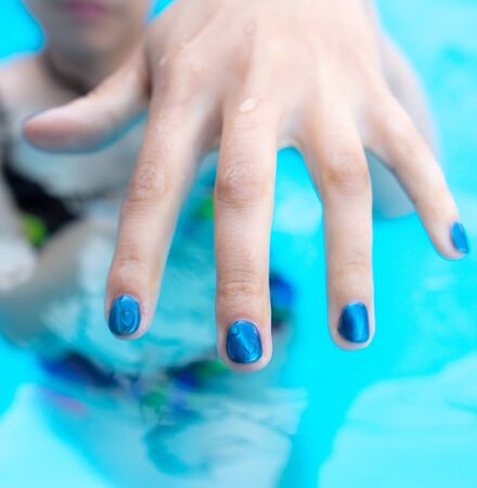 Hands of a girl with blue manicure in the water of the pool .の写真素材