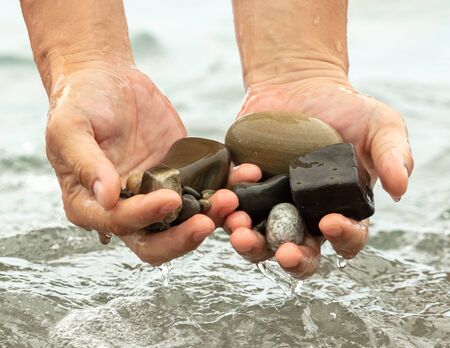 Stone pebbles in the hands of a man in the water of the sea .の写真素材