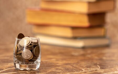 Coins in a glass cup on the background of old books .の写真素材