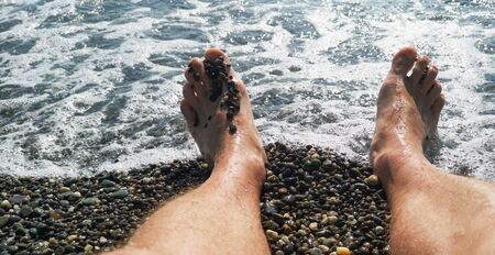 Men's feet on a pebble beach by the sea .の写真素材