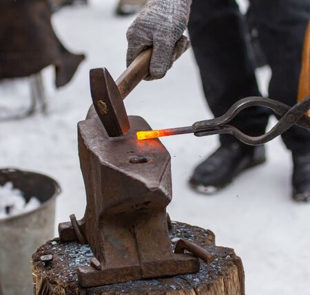 A blacksmith bends metal with a hammer.