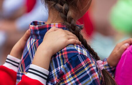 Hands on the shoulders of a girl with pigtails. Children play in the parkの写真素材
