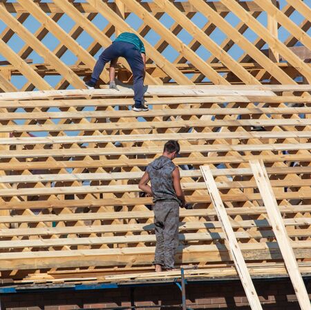 Workers are building the roof of the house from wood.