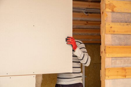 A worker fastens a sheet of drywall to the wall.の写真素材