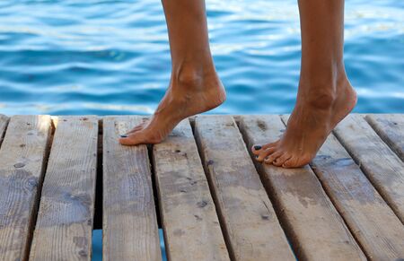 Legs of a girl on a wooden floor and a view of the blue sea.の写真素材