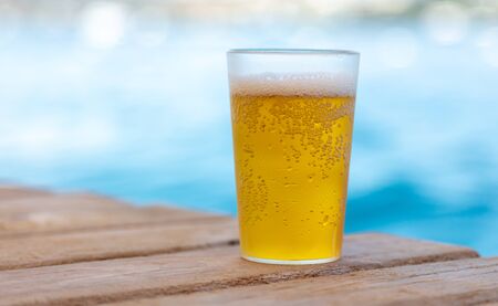 Glass with beer near the water on the beach.