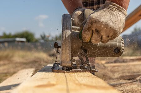 A worker cuts a wooden board at a construction site.の写真素材