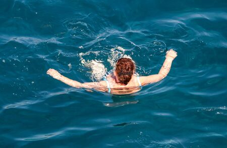 A girl swims in the blue water of the sea.の写真素材