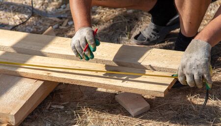 Worker measures a wooden board at a construction site.の写真素材