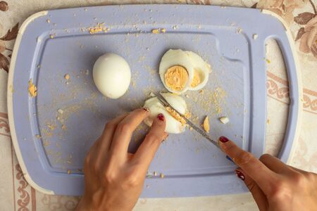 The girl cuts a boiled egg with a knife.