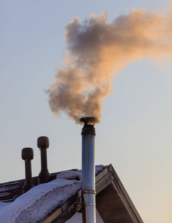 Smoke from the chimney of a house at dawn of the sun in winter.の写真素材