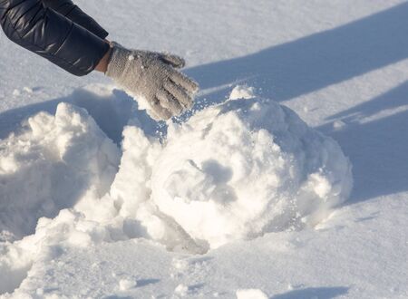Girl sculpts a snowman in the snow in winter.