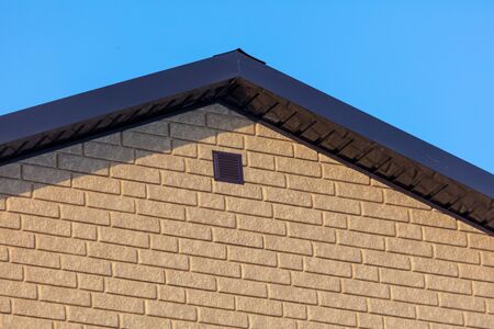 Roof in a brick house on a background of blue sky.