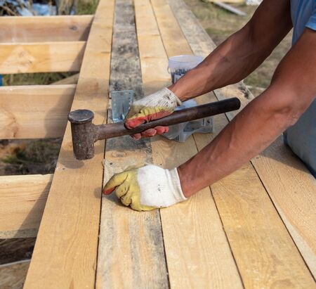 Work hammer a nail in a wooden beam at a construction site.